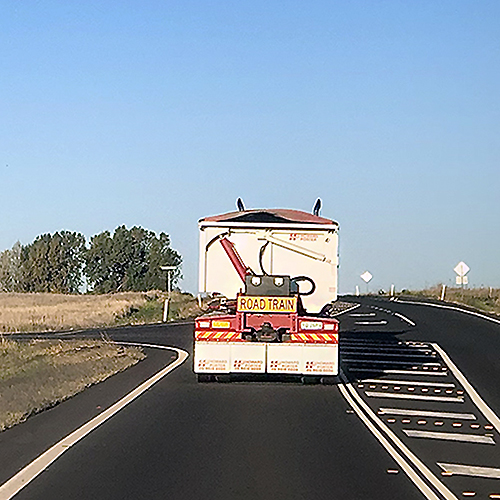 Out ahead through the windshield, the rear of a road train blocks the view of the open road as we crest a hill, making one vulnerable to the sudden surprise of who knows what